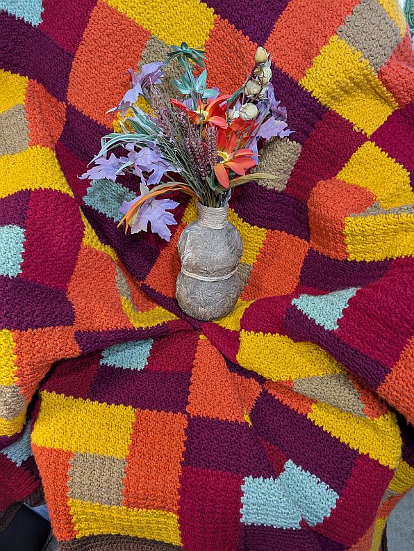 Textured crochet afghan in autumn colors arranged around a rustic vase of fall leaves and flowers