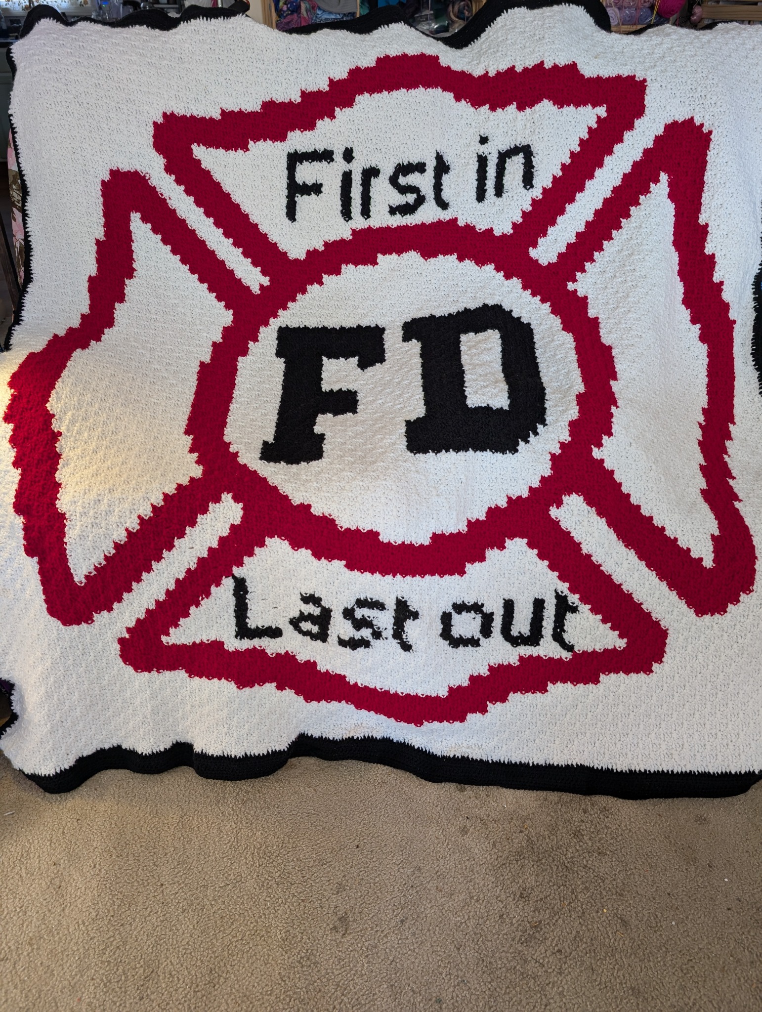 Hand-crocheted red, white, and black Maltese Cross afghan reading First in, Last out