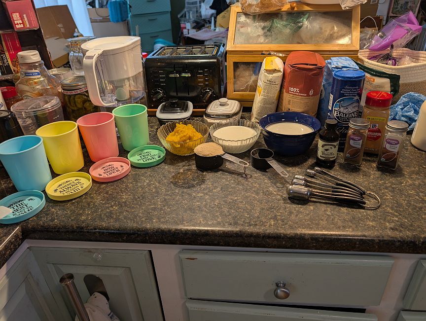 Pumpkin gelato ingredients, spices, bowls, and colorful serving cups arranged across a kitchen counter